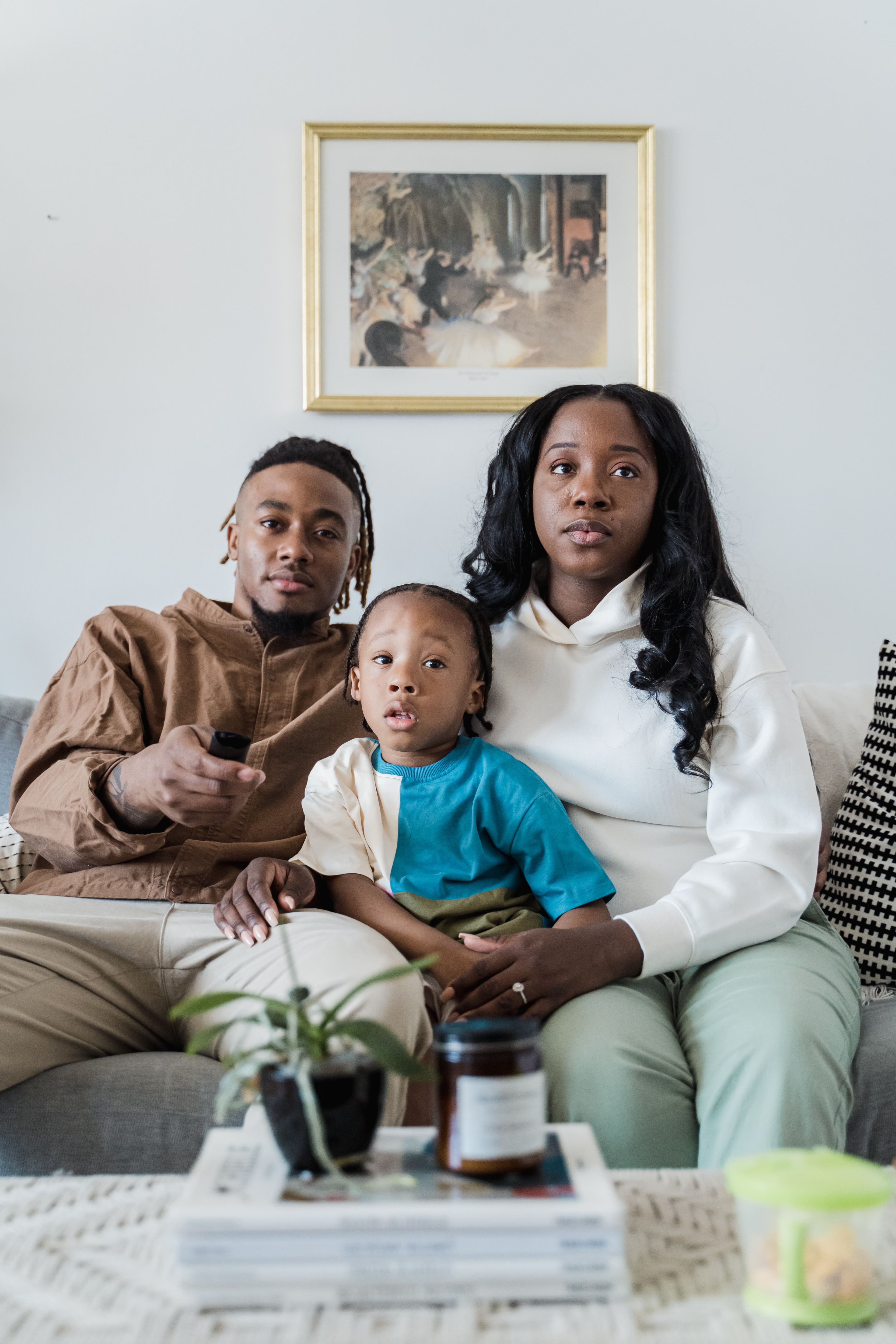 Family of three sitting together in a living room with a television remote.